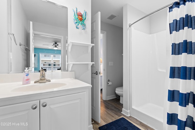 bathroom with hardwood / wood-style flooring, ceiling fan, vanity, toilet, and walk in shower