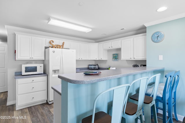 kitchen featuring white appliances, white cabinetry, ornamental molding, a kitchen bar, and kitchen peninsula
