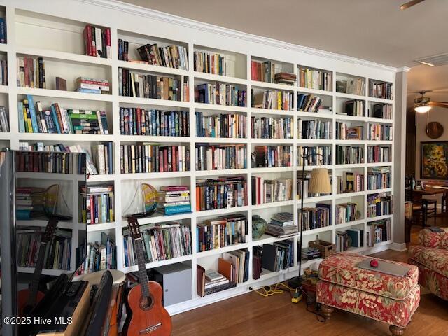 living area with a ceiling fan, visible vents, bookshelves, and wood finished floors