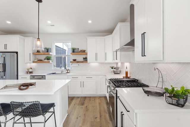 kitchen featuring pendant lighting, white cabinetry, sink, stainless steel appliances, and wall chimney exhaust hood