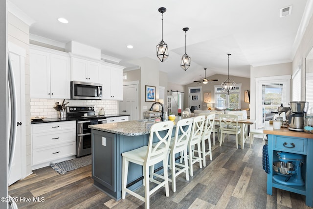 kitchen with a center island with sink, appliances with stainless steel finishes, pendant lighting, a barn door, and white cabinets