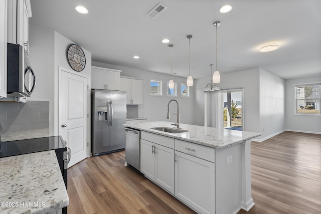 kitchen with sink, stainless steel appliances, light stone countertops, a kitchen island with sink, and white cabinets