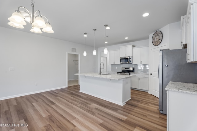 kitchen with appliances with stainless steel finishes, an island with sink, hanging light fixtures, and white cabinets