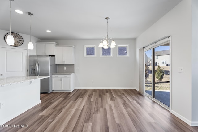 kitchen featuring stainless steel fridge, light stone countertops, hanging light fixtures, and white cabinets