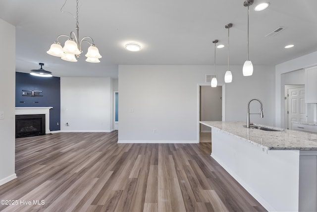 kitchen featuring sink, hardwood / wood-style flooring, hanging light fixtures, light stone counters, and white cabinets