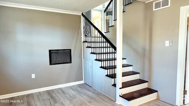 stairs with ornamental molding, hardwood / wood-style floors, and a textured ceiling