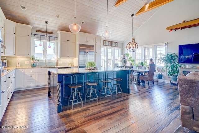 kitchen with white cabinetry, a center island, a kitchen breakfast bar, built in fridge, and pendant lighting