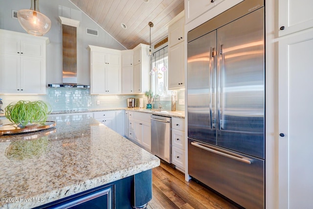 kitchen with appliances with stainless steel finishes, white cabinetry, lofted ceiling, hanging light fixtures, and wall chimney range hood