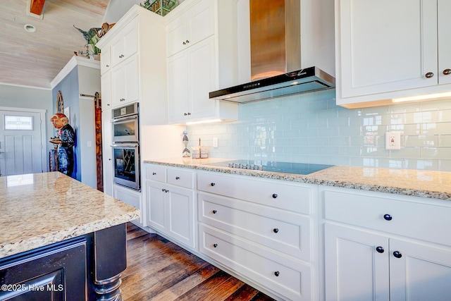 kitchen featuring wall chimney range hood, white cabinetry, double oven, light stone counters, and black electric cooktop