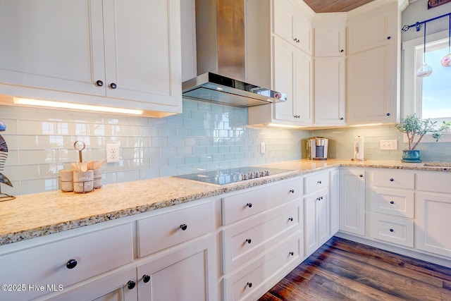 kitchen with black electric stovetop, white cabinets, light stone countertops, and wall chimney exhaust hood