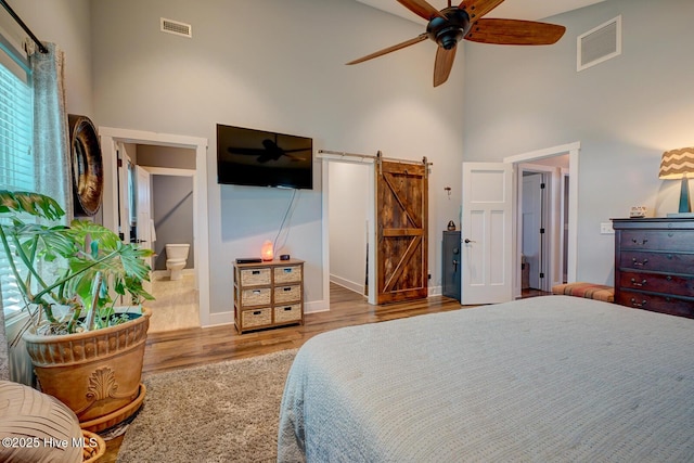 bedroom with ceiling fan, a high ceiling, connected bathroom, light hardwood / wood-style floors, and a barn door