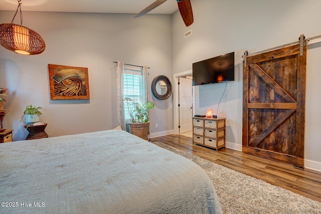 bedroom featuring hardwood / wood-style flooring, a towering ceiling, a barn door, and ceiling fan