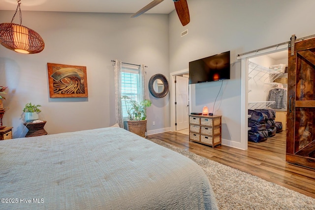 bedroom featuring ceiling fan, high vaulted ceiling, wood-type flooring, a walk in closet, and a barn door