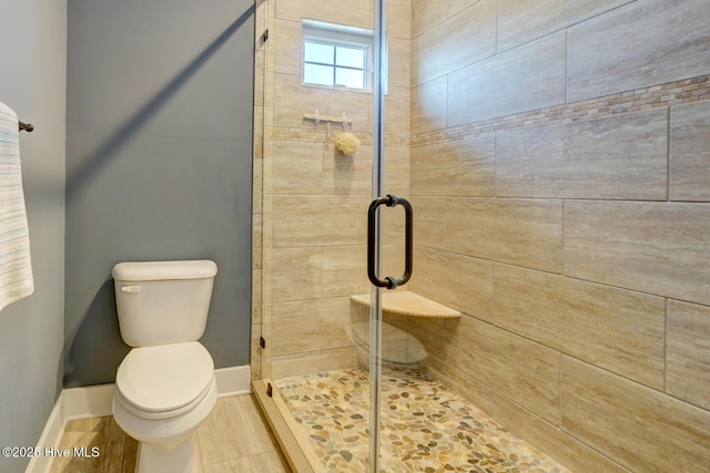 bathroom featuring a shower with door and toilet