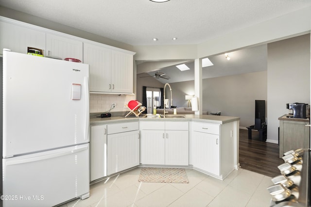 kitchen with tasteful backsplash, white cabinetry, sink, white fridge, and kitchen peninsula