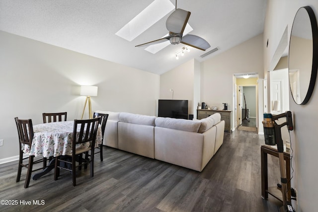 living room with a skylight, high vaulted ceiling, dark hardwood / wood-style floors, and ceiling fan