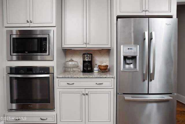 kitchen featuring wood finished floors, light stone countertops, stainless steel appliances, white cabinets, and backsplash