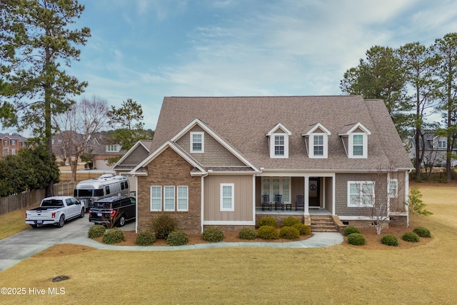 view of front facade with a front lawn, fence, roof with shingles, covered porch, and concrete driveway