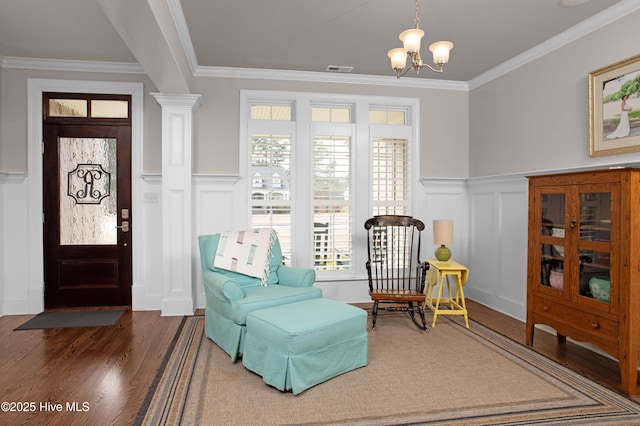 sitting room with an inviting chandelier, wood finished floors, crown molding, and a decorative wall