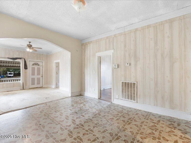 empty room with crown molding, ceiling fan, a textured ceiling, and wood walls