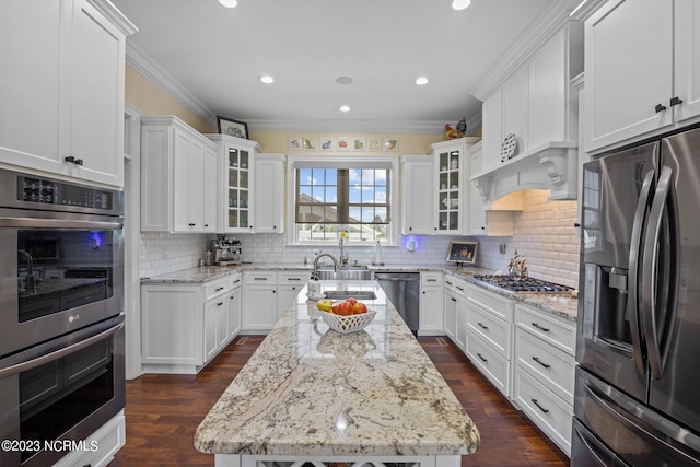 kitchen featuring light stone counters, crown molding, a center island, appliances with stainless steel finishes, and white cabinets