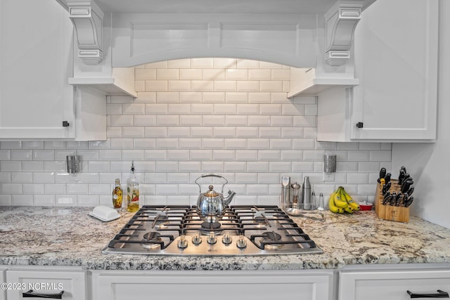 kitchen with light stone counters, decorative backsplash, stainless steel gas stovetop, and white cabinets