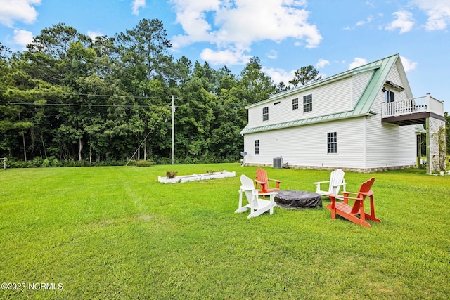 back of property with central AC unit, a lawn, and an outdoor fire pit