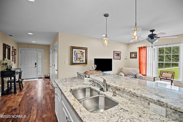 kitchen with dark wood-type flooring, sink, light stone counters, hanging light fixtures, and white cabinets