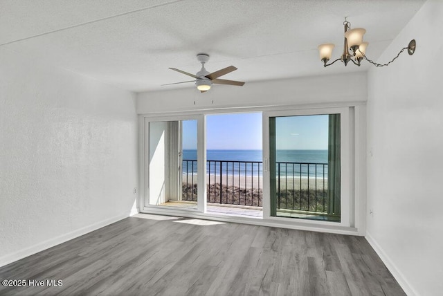 unfurnished room with a textured ceiling, wood-type flooring, a beach view, and a water view