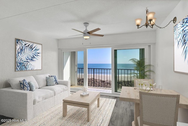 living room with hardwood / wood-style floors, a water view, a beach view, a textured ceiling, and ceiling fan with notable chandelier