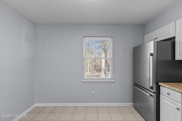 kitchen with white cabinetry, stainless steel fridge, a textured ceiling, and light tile patterned floors