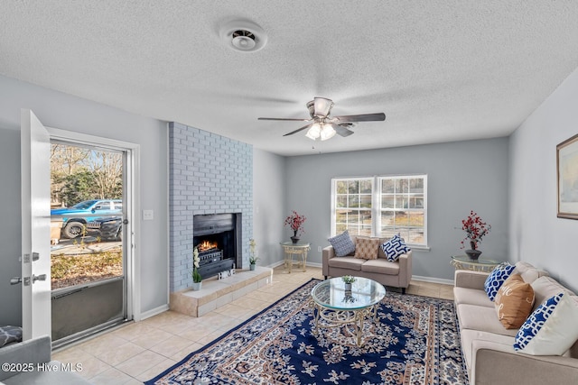 living room featuring a brick fireplace, a textured ceiling, ceiling fan, and light tile patterned flooring