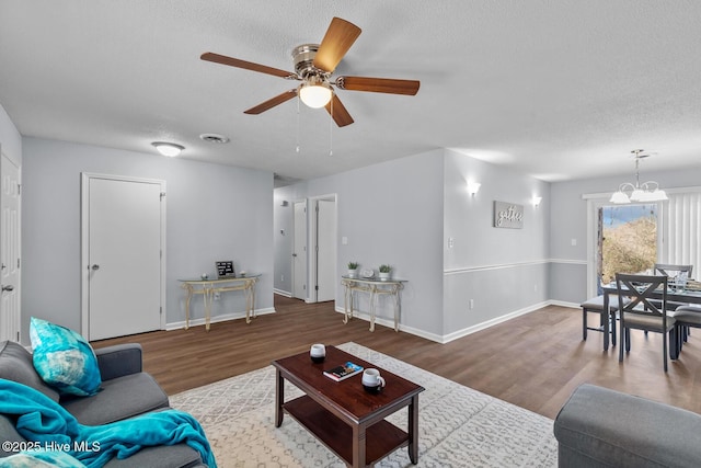 living room with hardwood / wood-style flooring, ceiling fan with notable chandelier, and a textured ceiling