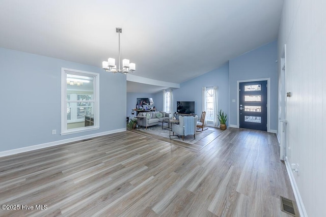 unfurnished living room with vaulted ceiling, an inviting chandelier, and light wood-type flooring