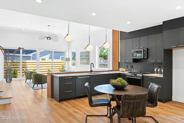 kitchen with pendant lighting, sink, appliances with stainless steel finishes, light hardwood / wood-style floors, and decorative backsplash