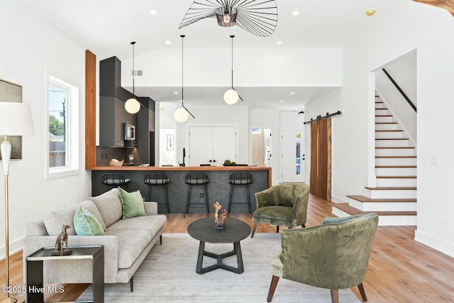 living room with vaulted ceiling, a barn door, sink, and light hardwood / wood-style flooring