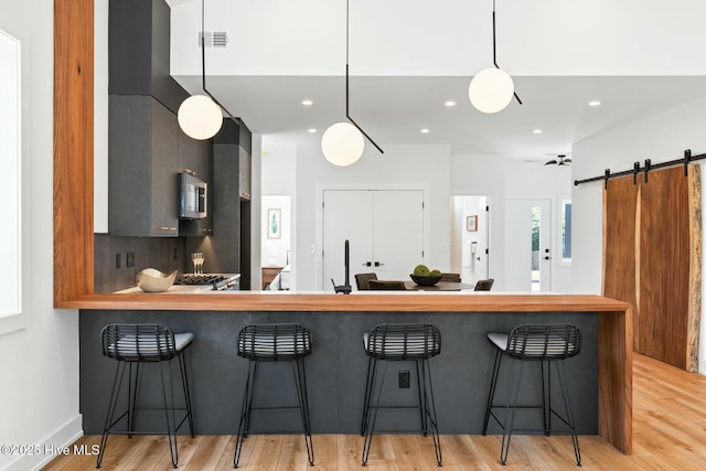 kitchen featuring a kitchen breakfast bar, hanging light fixtures, light hardwood / wood-style floors, kitchen peninsula, and a barn door