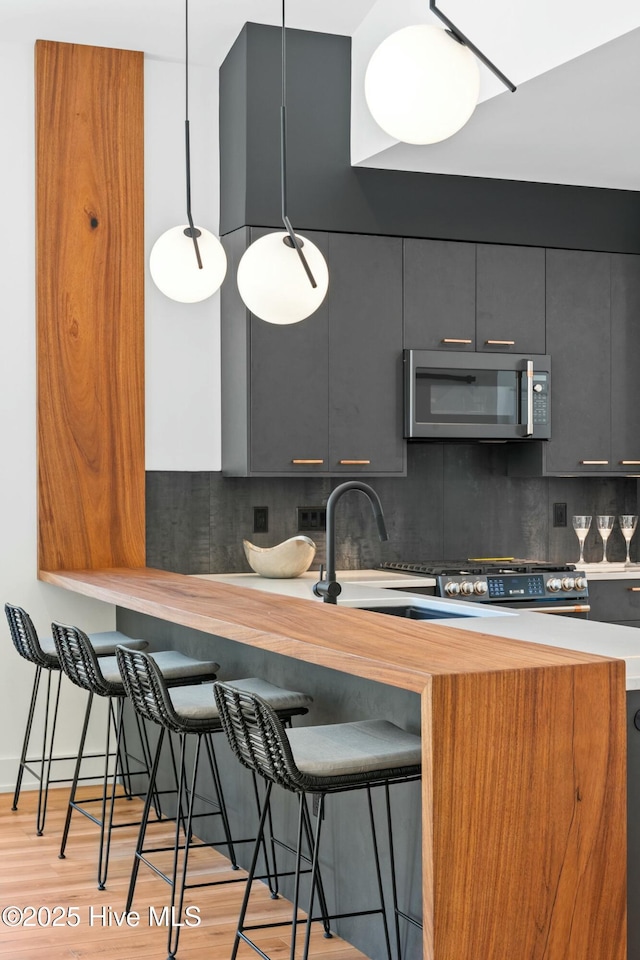 kitchen featuring light hardwood / wood-style floors, decorative backsplash, a kitchen bar, decorative light fixtures, and kitchen peninsula