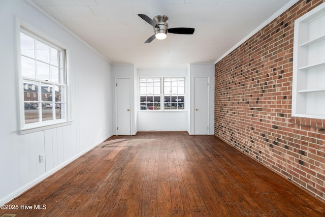 empty room with ornamental molding, dark hardwood / wood-style flooring, built in features, ceiling fan, and brick wall