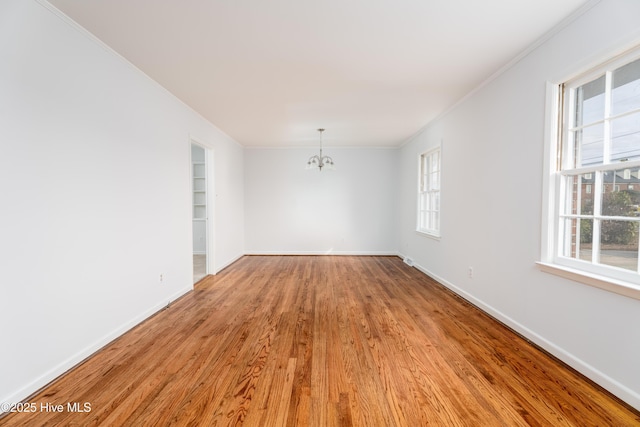 spare room featuring ornamental molding, plenty of natural light, light wood-type flooring, and a notable chandelier