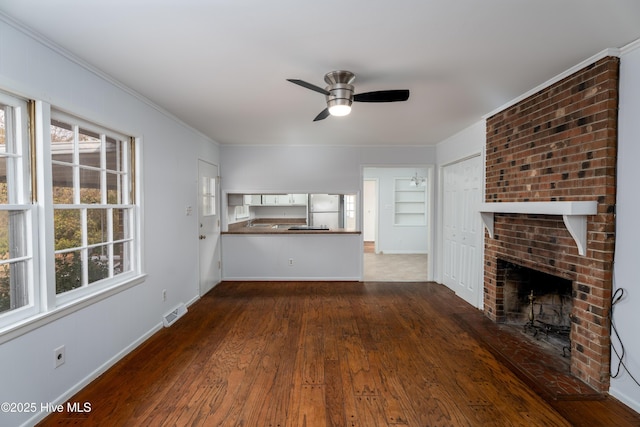 unfurnished living room with dark wood-type flooring, built in features, ceiling fan, a fireplace, and ornamental molding