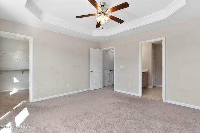 unfurnished bedroom with ensuite bathroom, crown molding, a walk in closet, light carpet, and a raised ceiling