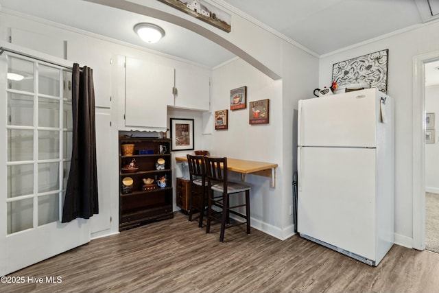 kitchen with white refrigerator, white cabinetry, hardwood / wood-style flooring, and crown molding