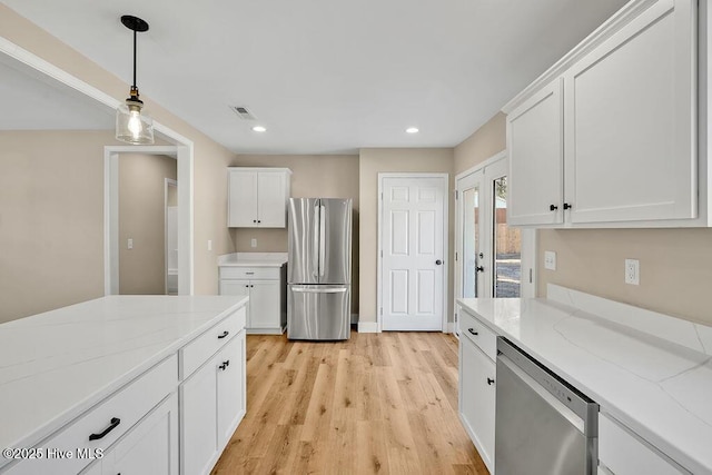 kitchen with appliances with stainless steel finishes, pendant lighting, white cabinets, light stone counters, and light wood-type flooring