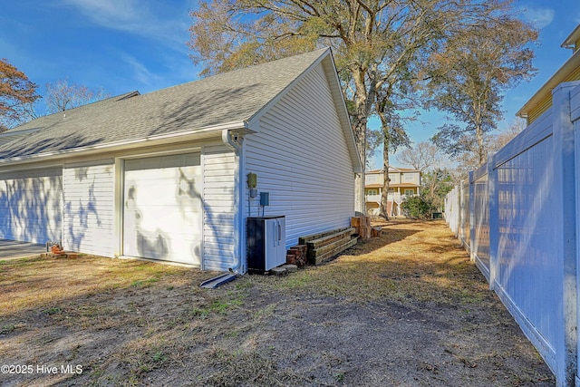 view of side of property featuring a garage, roof with shingles, an outdoor structure, and fence