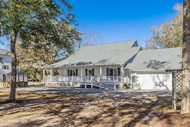 view of front of property featuring a storage unit, driveway, a porch, roof with shingles, and an attached garage