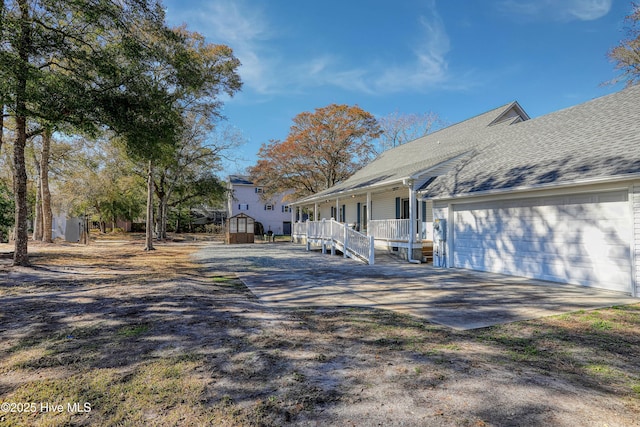 view of property exterior with a shed, driveway, a porch, an attached garage, and a shingled roof