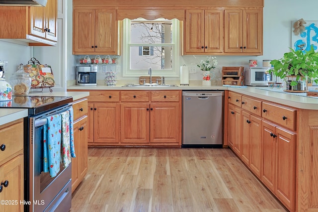 kitchen with light wood finished floors, light countertops, a peninsula, stainless steel appliances, and a sink