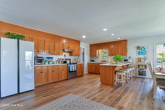 kitchen featuring light wood-style flooring, under cabinet range hood, white appliances, a breakfast bar area, and light countertops