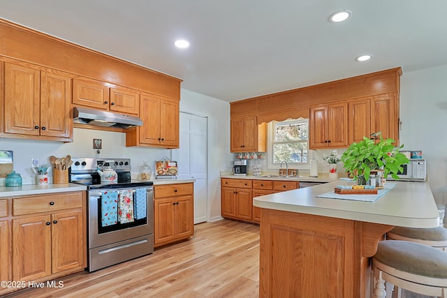 kitchen with a peninsula, light countertops, light wood-style floors, under cabinet range hood, and appliances with stainless steel finishes